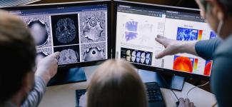 Three researchers looking at brain scans on two computer screens